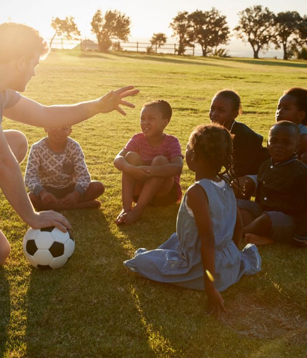 Elementary school kids and teacher sitting with ball in field
